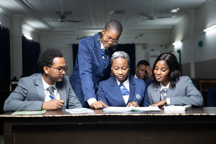 Quatre étudiants en blazer bleu réunis autour d’une table de travail, penchés sur un même document.